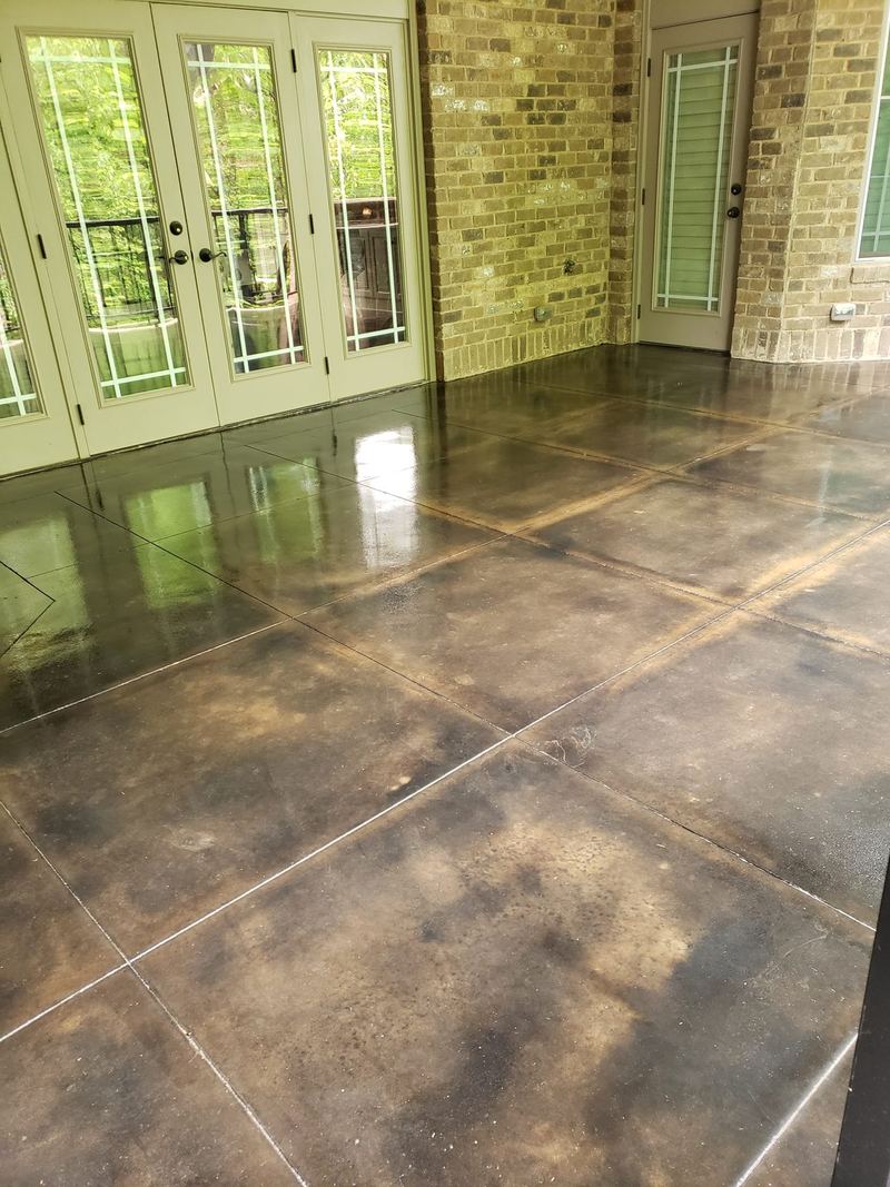 Glossy stained concrete patio floor in front of white French doors and stone columns