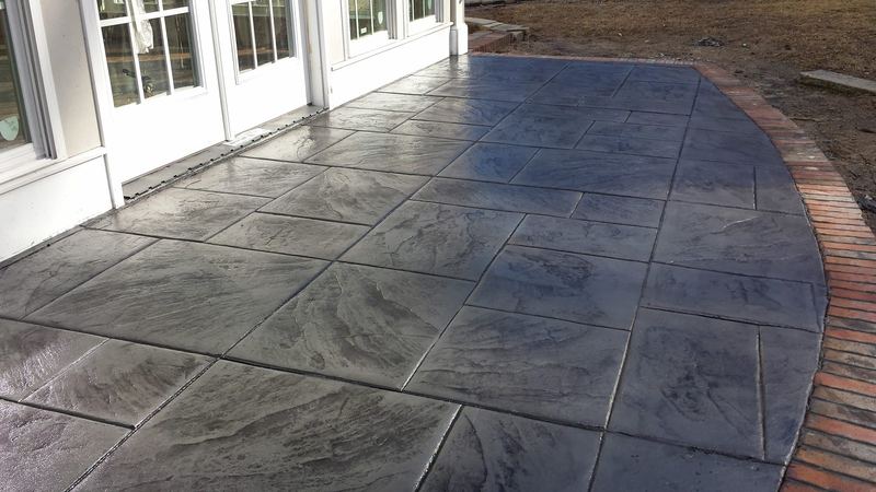Gray stamped slate-pattern concrete patio with a curved brick-pattern border